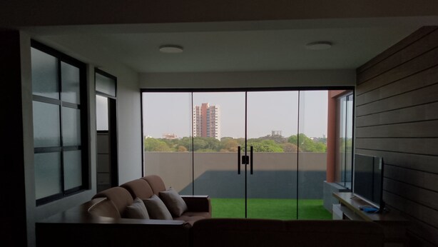 A modern living room with a sofa, a television, and a view of a cityscape through large windows.