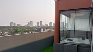 A balcony with artificial grass, a glass-enclosed bathroom, and a cityscape view.