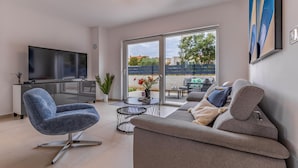 A modern living room with a flat-screen TV, a blue armchair, a grey sofa, and a glass door leading to an outdoor area. - Awesome home in Liznjan (Liznjan)