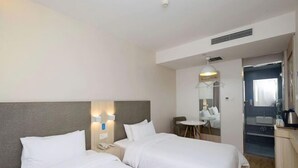 Habitación de hotel con dos camas, un escritorio, una silla, un espejo y un baño visible a través de una puerta abierta.