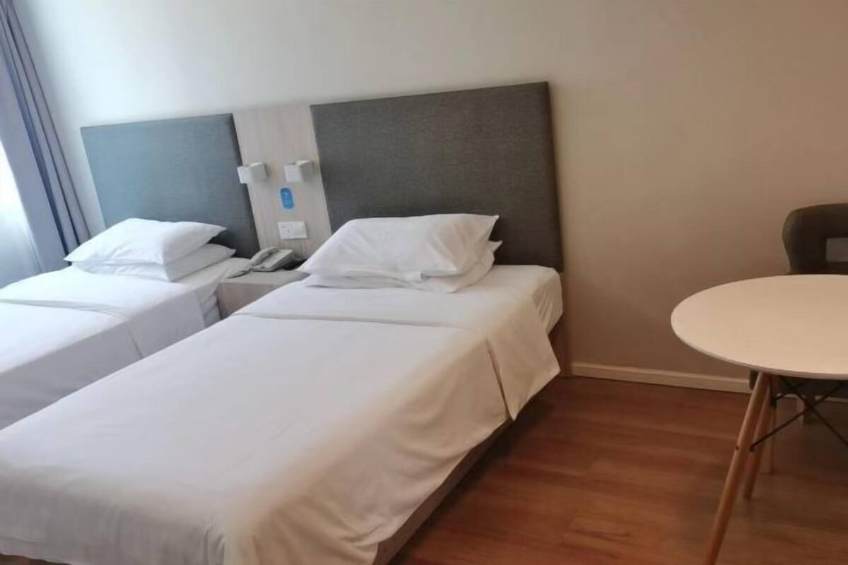 Une chambre d’hôtel avec deux lits simples, une table de chevet, une table ronde et un téléphone fixé au mur.