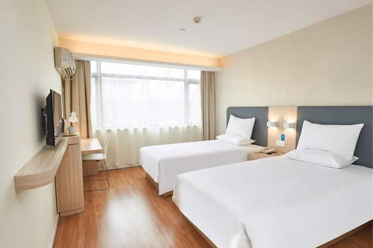Une chambre d’hôtel avec deux lits, un bureau, une télévision et une fenêtre avec des rideaux.