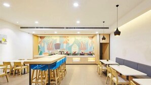 Un comedor moderno con mesas y sillas de madera, una isla central con mantel azul y un mural colorido en la pared de fondo.