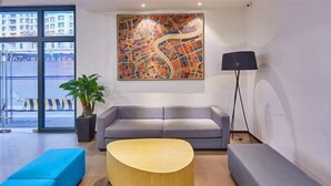 Un vestíbulo moderno con un sofá gris, una mesa redonda de madera y un cuadro abstracto grande en la pared.