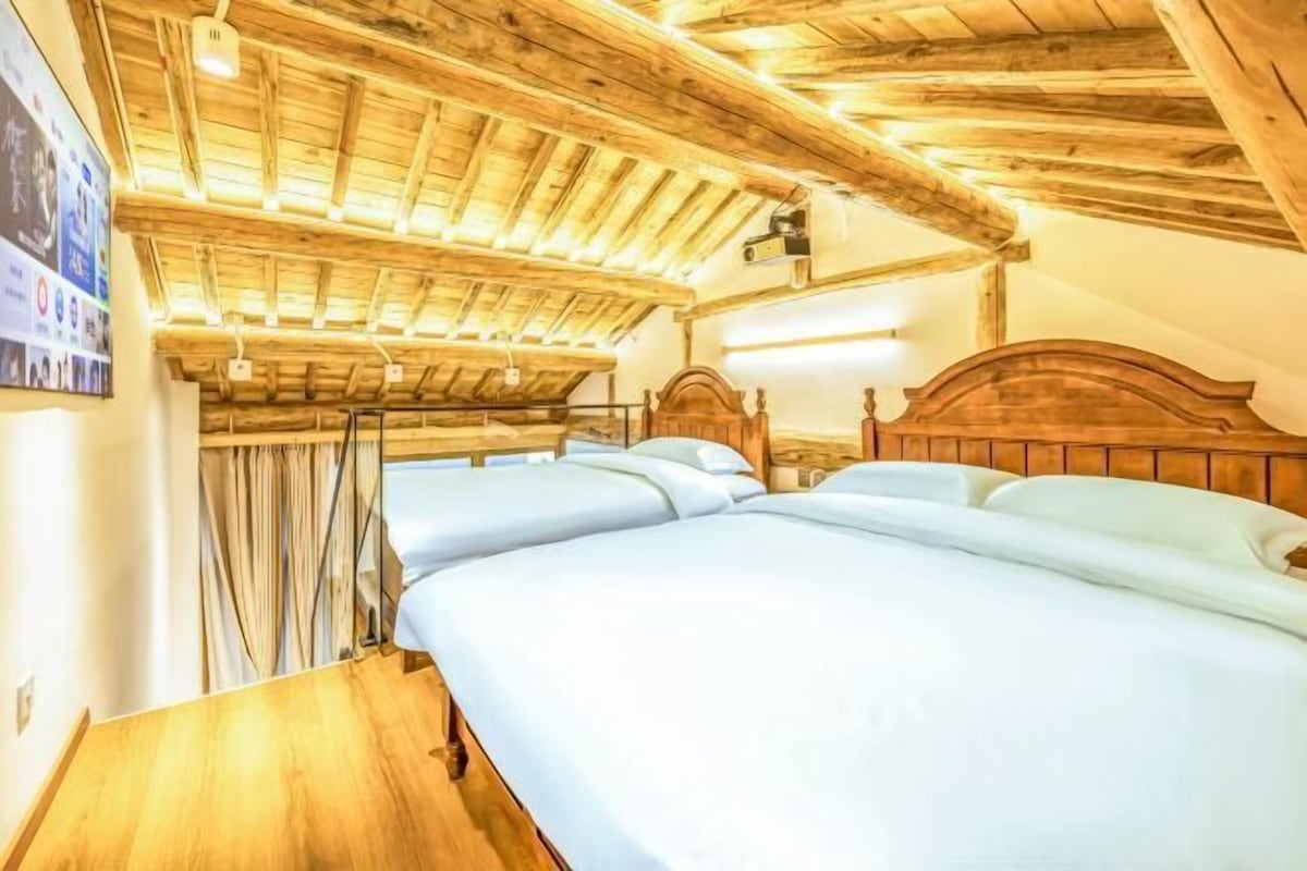 Ein Zimmer mit Holzbalkendecke und geneigtem Dach, ausgestattet mit zwei Betten und Holz Kopfteilen sowie weißer Bettwäsche.
