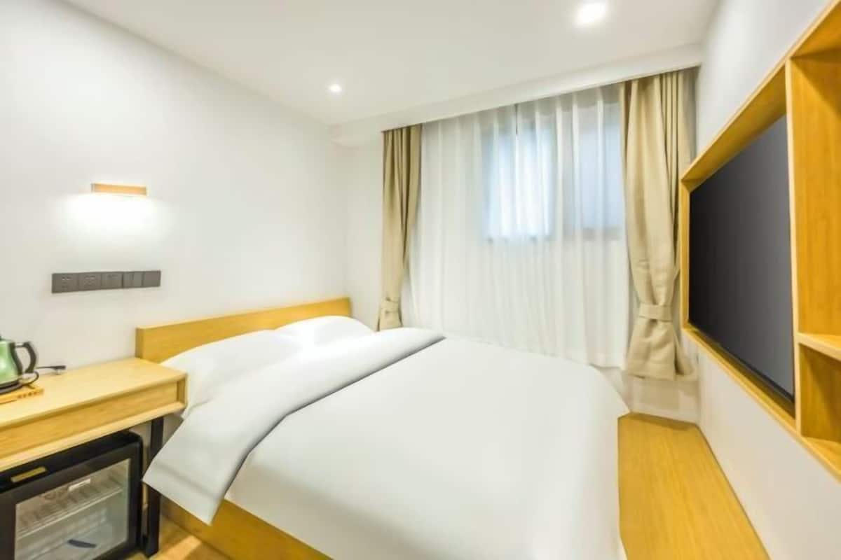 Une chambre d’hôtel avec un lit, un bureau doté d’une bouilloire, une télévision et une fenêtre avec des rideaux.