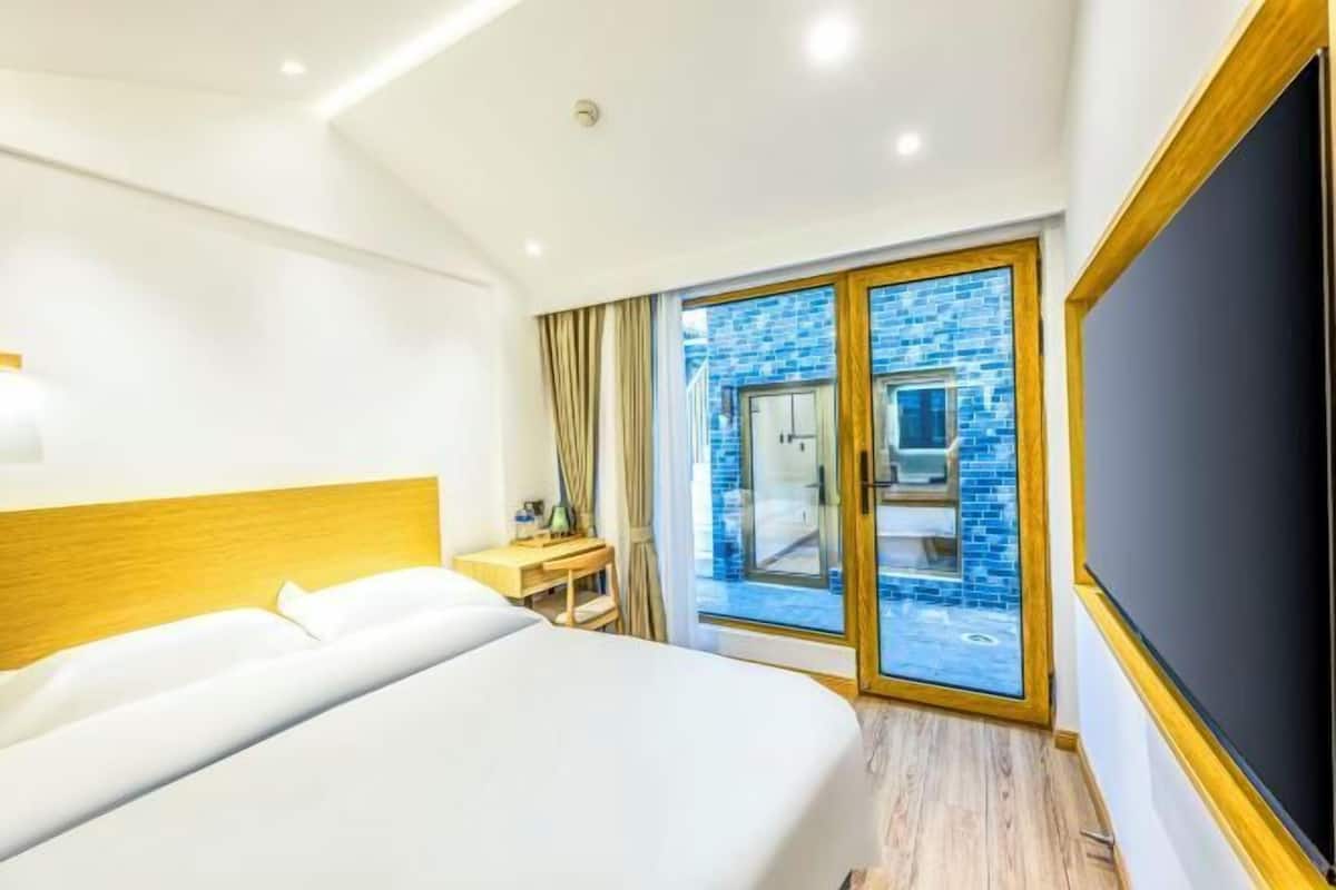 Une chambre d’hôtel avec un grand lit, un bureau et une télévision. Une porte-fenêtre coulissante donne sur un espace extérieur agrémenté d’un mur en briques bleues.