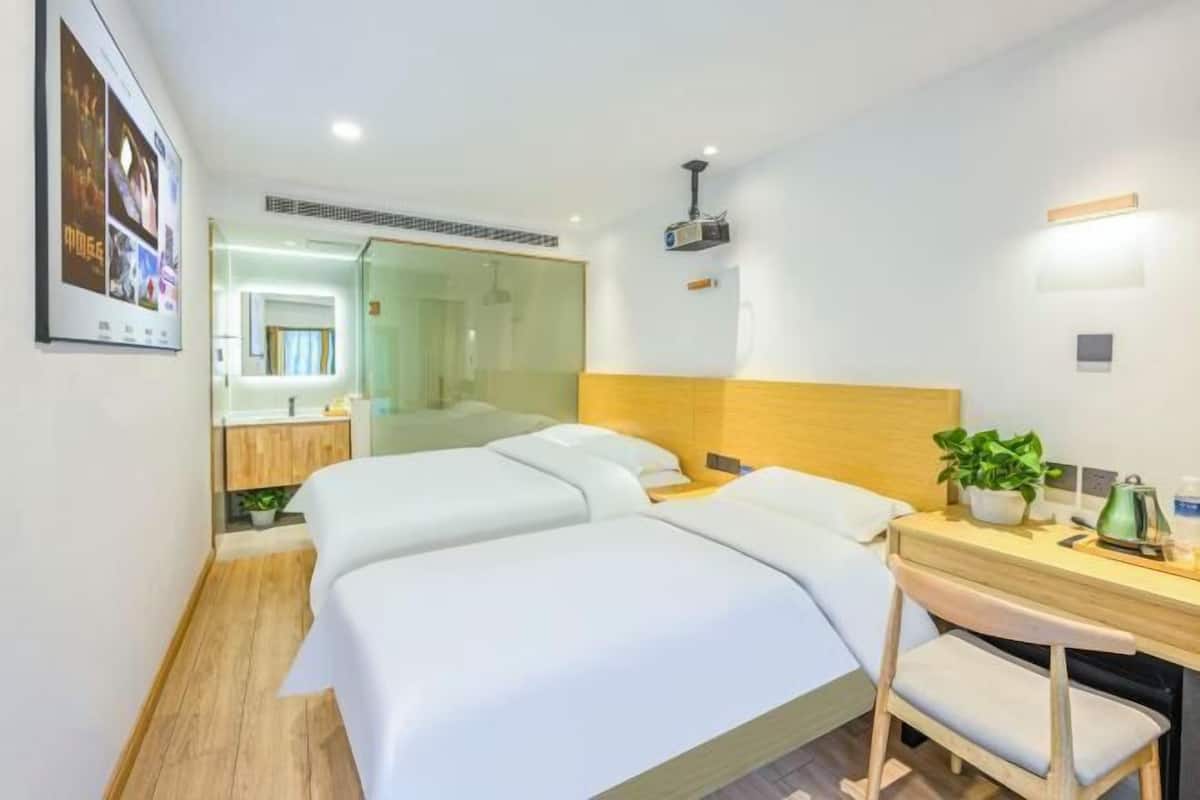 Une chambre d’hôtel moderne avec un grand lit, un bureau avec une chaise, une petite table avec une plante et un projecteur fixé au plafond.
