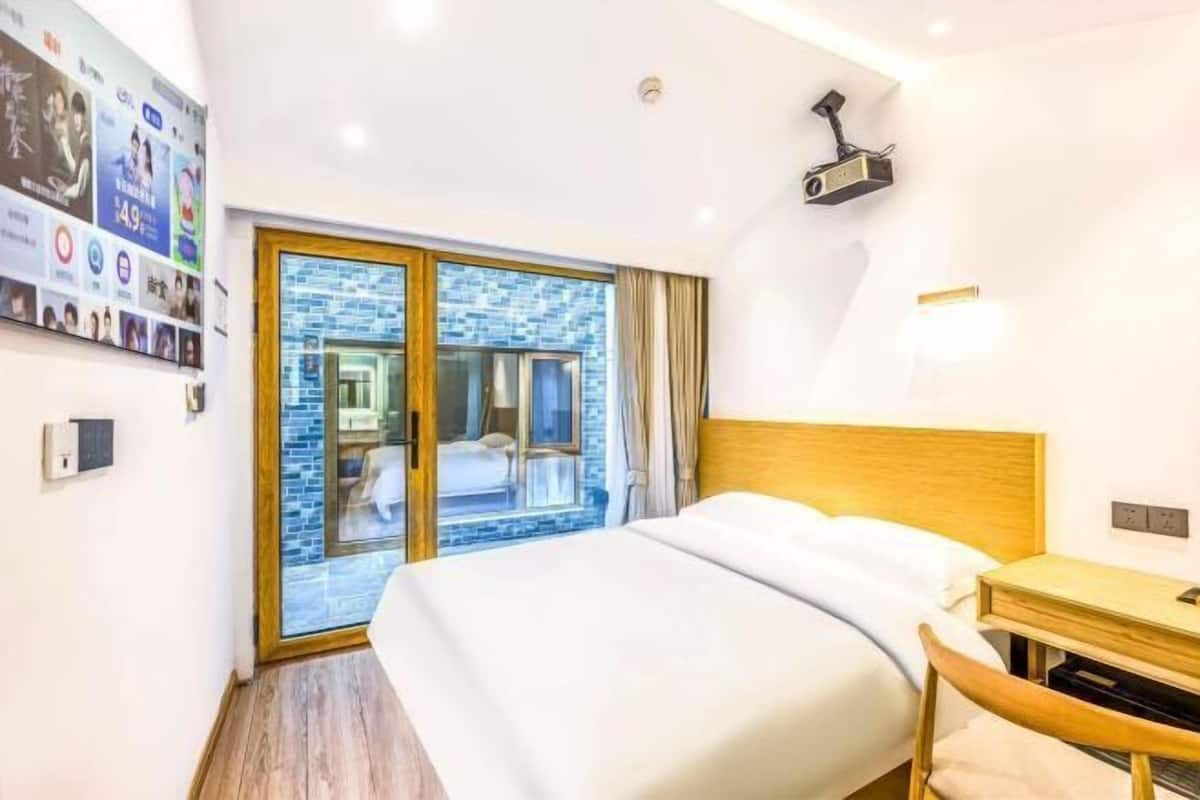 Une chambre d’hôtel avec un grand lit, une tête de lit en bois, un bureau et une porte-fenêtre coulissante donnant sur un balcon.