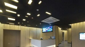 Un espace d’accueil d’hôtel au design moderne, comprenant un comptoir d’accueil, un écran numérique affichant le nom de l’hôtel et un sol carrelé.