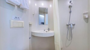 Une petite salle de bain propre, équipée d’un lavabo, d’un miroir et d’une douche.