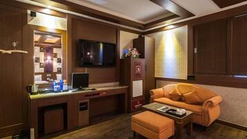 A hotel room with a wooden desk, a flat-screen TV, a sofa, and a small table.