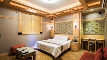 A hotel room with a bed, bedside table, chair, desk, and a window with blinds.