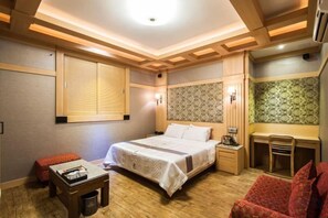A hotel room with a bed, bedside table, chair, desk, and a window with blinds. - Aura Tourist Hotel (Ansan)