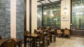 Interior de restaurante com mesas e cadeiras de madeira, painéis decorativos e vista através de uma janela estampada.