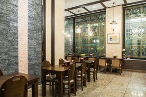 A restaurant interior with wooden tables and chairs, decorative wall panels, and a view through a patterned window. - Aura Tourist Hotel (Ansan)