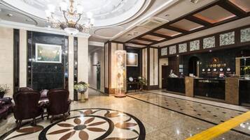 Um hall de hotel com balcão de recepção, área de estar e um padrão decorativo no chão.