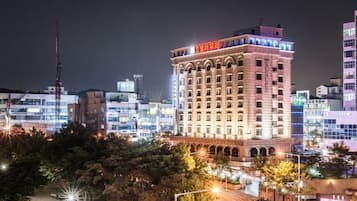 Um hotel com vários andares e uma placa vermelha grande no topo, cercado por outros edifícios.