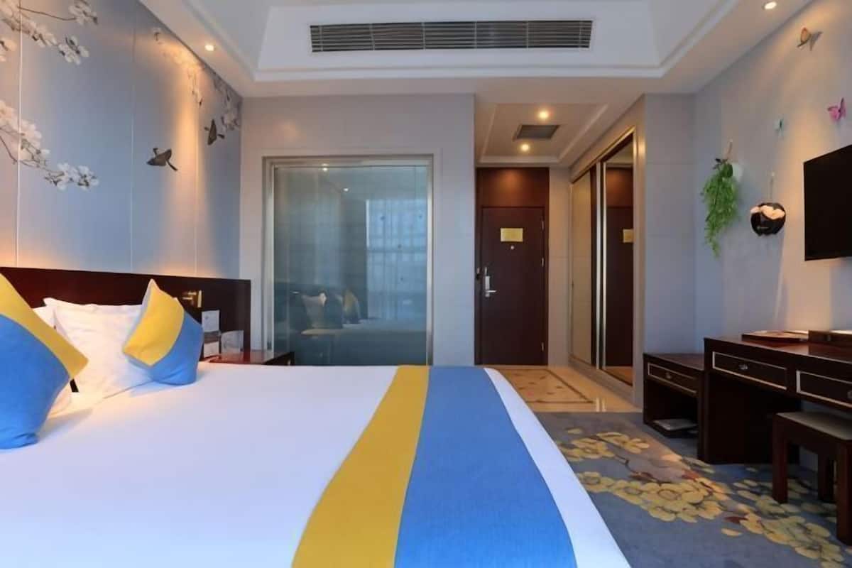 A hotel room with a bed, a desk, a television, and a door leading to a bathroom.