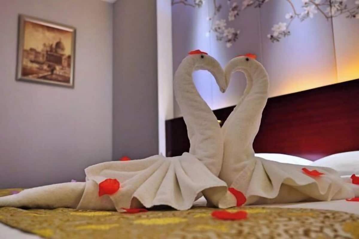 A bed with a decorative arrangement of two swan-shaped pillows and rose petals.