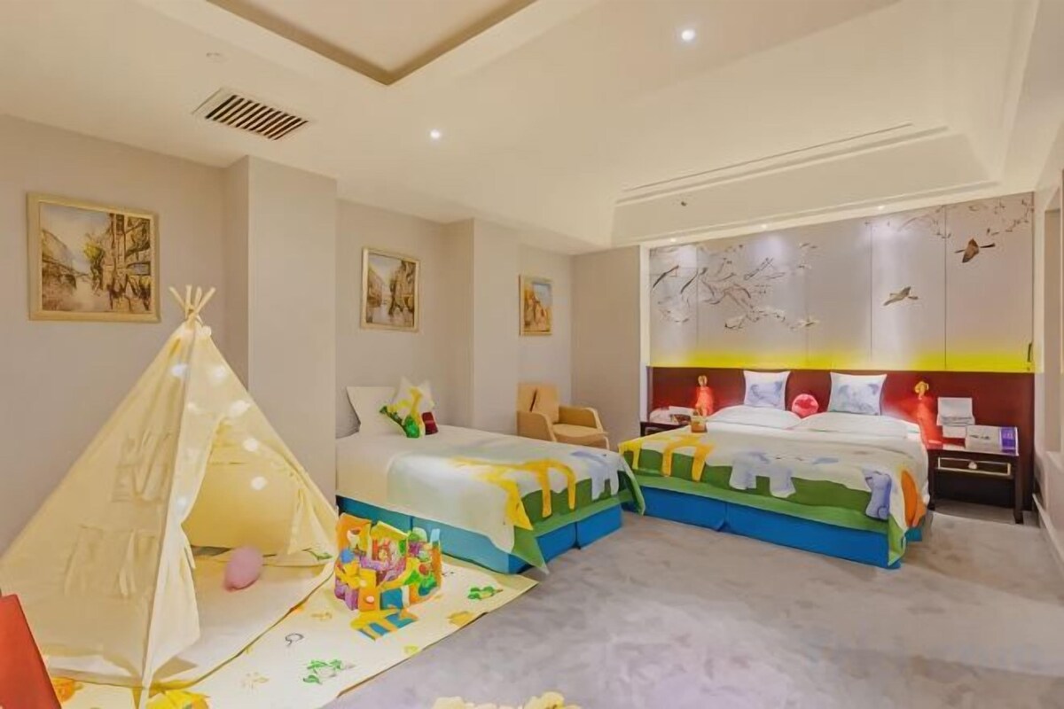 A bedroom with two beds, a play tent, and a wall with bird illustrations.