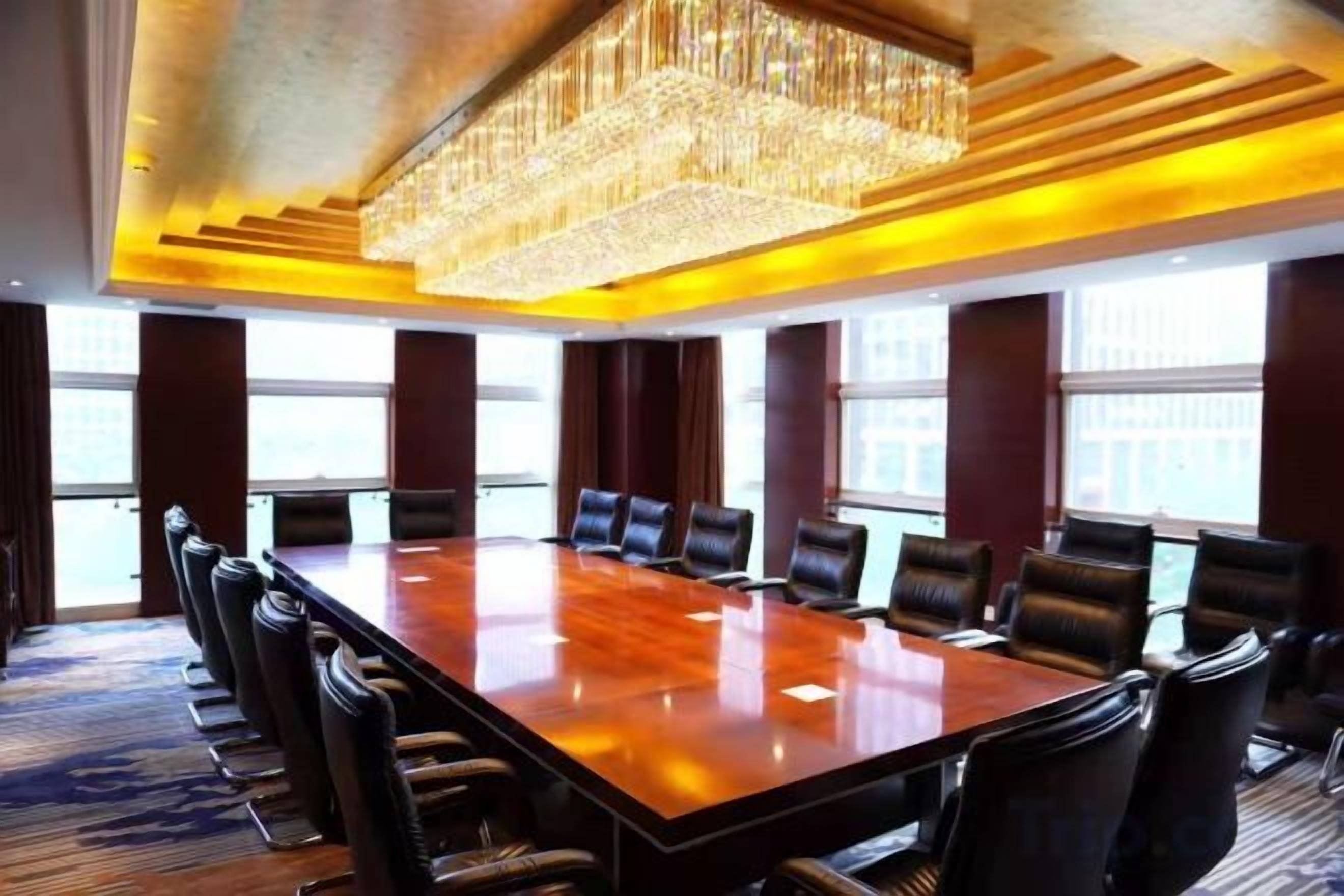 Une salle de conférence dotée d’une grande table rectangulaire entourée de chaises, d’un lustre et de grandes fenêtres.