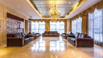 A spacious lobby with leather sofas, a chandelier, and large windows with curtains.