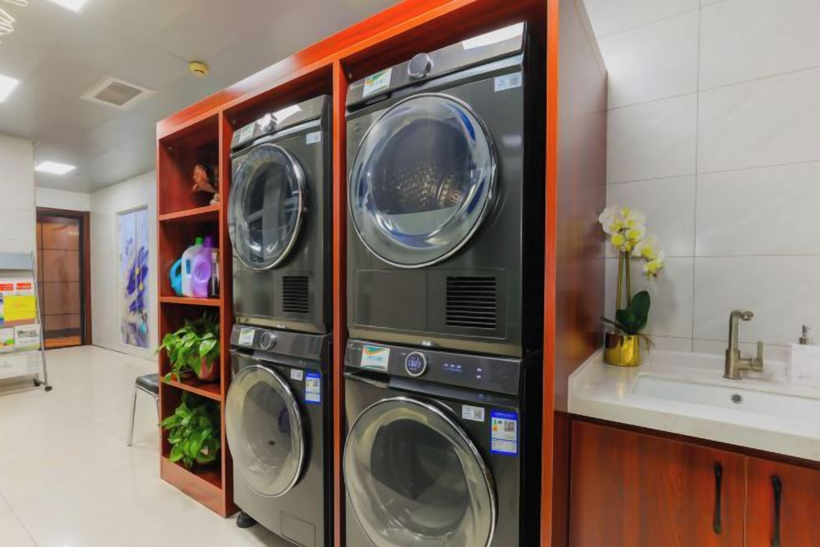 A laundry facility with multiple washing machines, a sink, and a shelf with folded clothes.