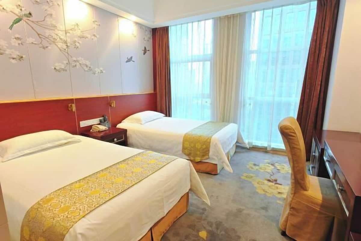 A hotel room with two beds, a desk, a chair, and a large window with curtains.