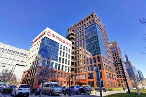 A modern building with a glass facade, surrounded by parked cars and a clear blue sky. - Yangfeng Yiju Hotel (Beijing)