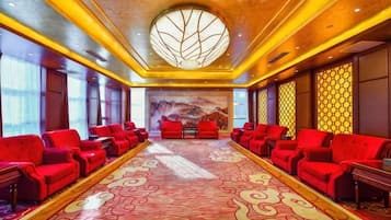 A conference room with red chairs arranged in rows, a patterned carpet, and a large circular window on the ceiling.
