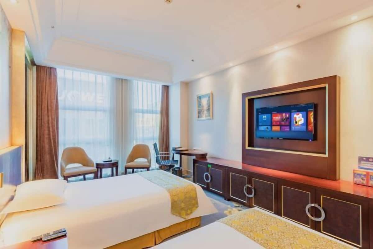 A hotel room with a bed, two chairs, a desk, a TV, and a large window.