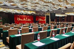 A conference room with rows of tables, chairs, and water bottles, with a red backdrop and a chandelier. - Yangfeng Yiju Hotel (Beijing)