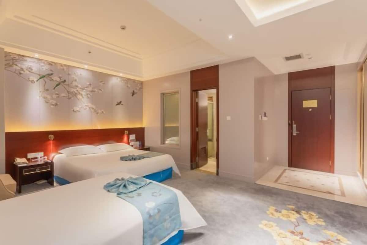 A hotel room with two beds, a decorative wall, a wooden door, and a carpet with a floral pattern.