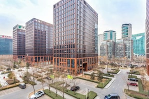 A high-rise building with a modern architectural design, surrounded by a landscaped area with trees and a parking lot. - Yangfeng Yiju Hotel (Beijing)