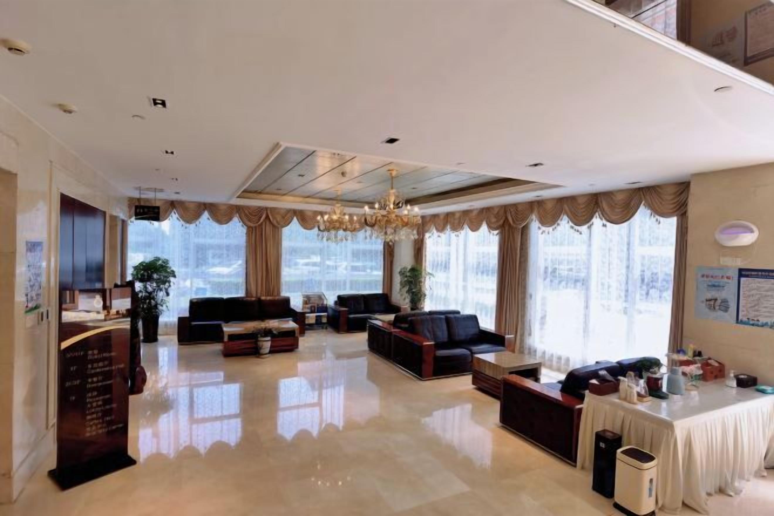 A spacious hotel lobby with a reception desk, seating area, and large windows offering a view of the city.