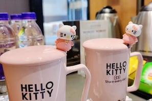 Zwei Hello Kitty Tassen mit Figuren darauf, auf einer Theke, im Hintergrund Wasserflaschen.