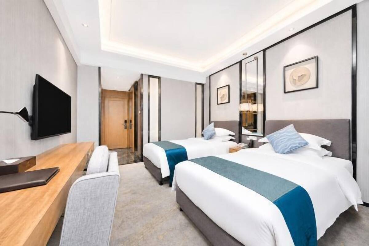 Une chambre d’hôtel avec deux lits, un bureau, une télévision et une porte donnant sur une salle de bain.