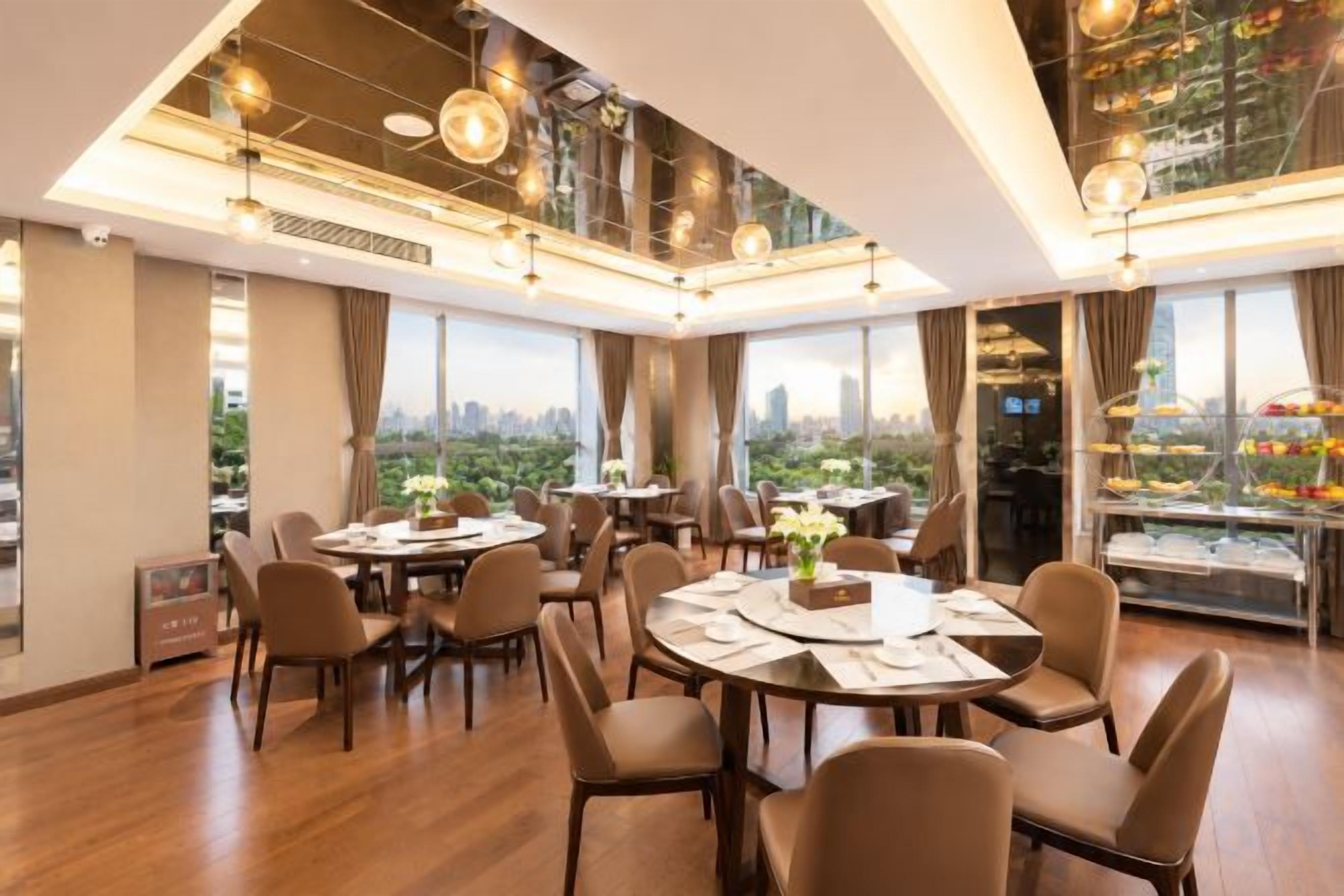 A modern dining area with multiple tables and chairs, large windows with a city view, and a decorative glass display case.