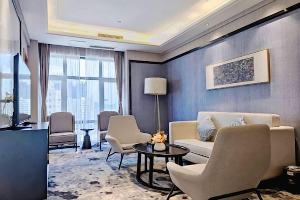Quarto de hotel moderno com sofá, poltronas, mesa de centro e vista para a cidade.