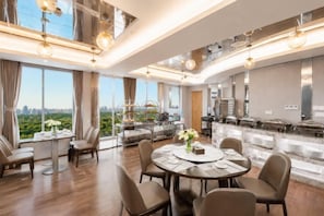 Une cuisine moderne dotée d’un grand îlot central, d’un coin repas avec une table ronde et offrant une vue sur la ville grâce à de grandes fenêtres.