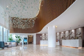Eine geräumige Lobby mit hoher Decke, einem Empfangstresen und einer großen Pflanze.