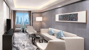 Une chambre d’hôtel moderne avec un canapé, des fauteuils, une table basse, un téléviseur et une vue sur la ville.