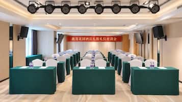 A conference room with rows of tables and chairs, a banner with text, and a stage with lighting.