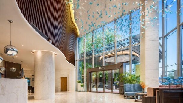 Un hall d’hôtel moderne avec un comptoir d’accueil, un espace salon et de grandes fenêtres.
