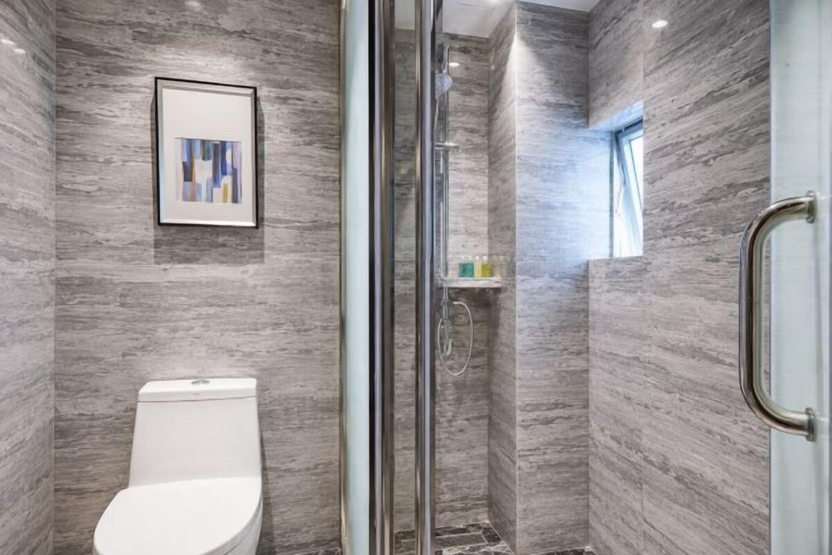 Une salle de bain avec une douche à parois de verre, des toilettes et une œuvre d’art encadrée au mur.