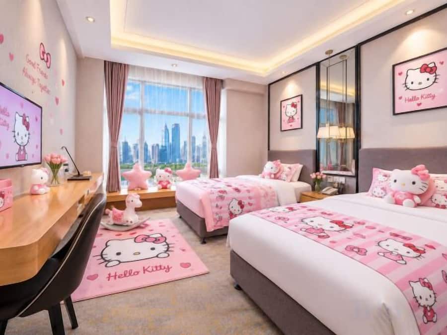 A hotel room with two beds, a desk, and a view of a cityscape.