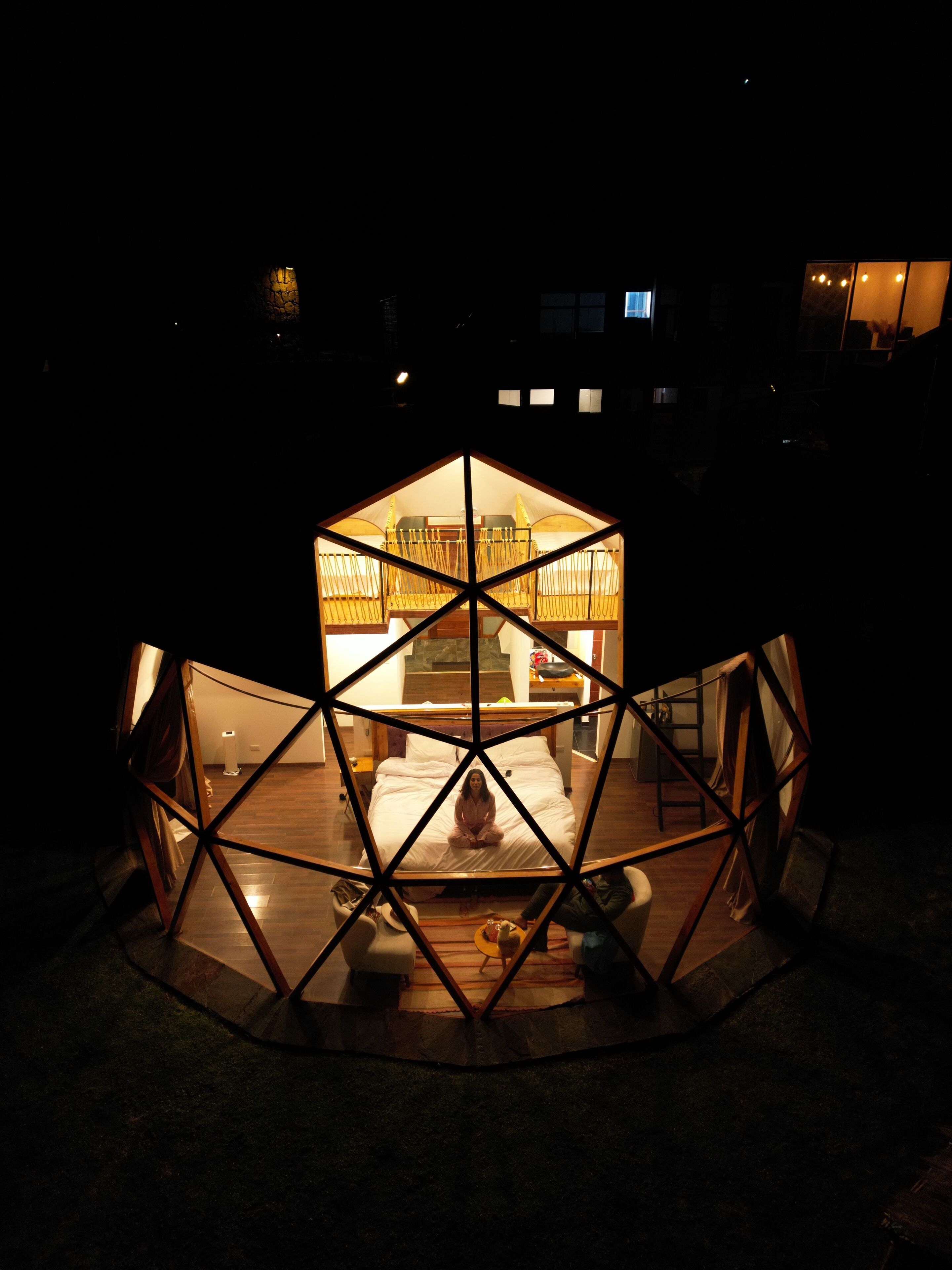 Una estructura tipo cúpula geodésica hexagonal con una cama central y una persona sentada en ella.