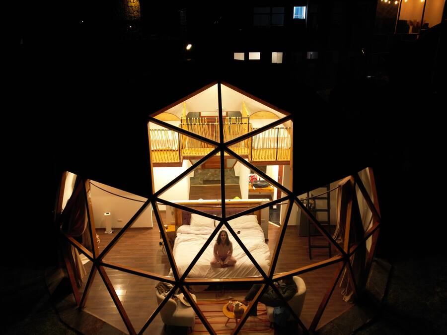 Una estructura tipo cúpula geodésica hexagonal con una cama central y una persona sentada en ella.