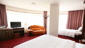 A hotel room with a large bed, a leather armchair, a desk with a TV, and a second bed. - Baile Hotel (Enping)